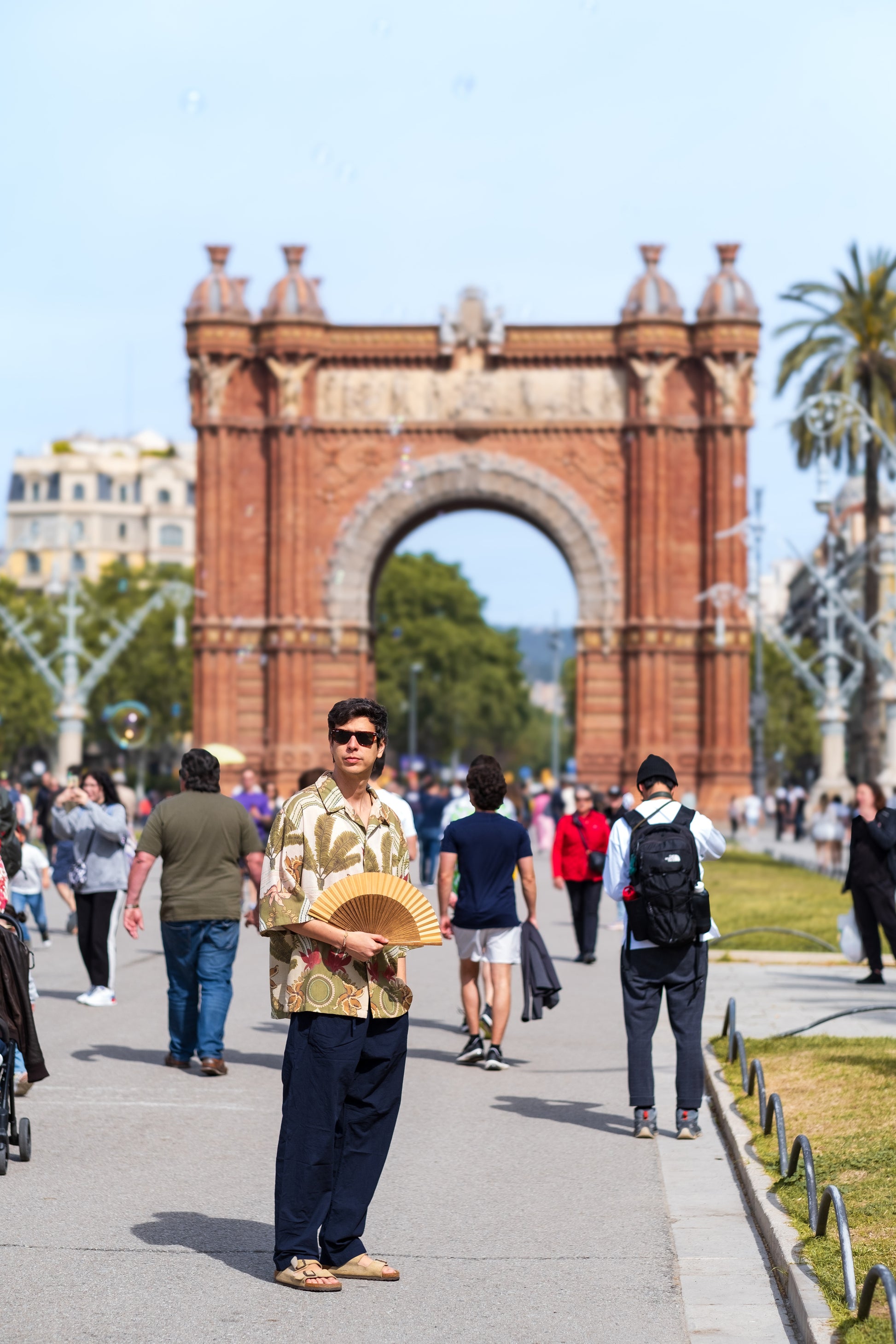 Hombre frente al arco del triunfo de Barcelona utilizando abanico color marron / camel