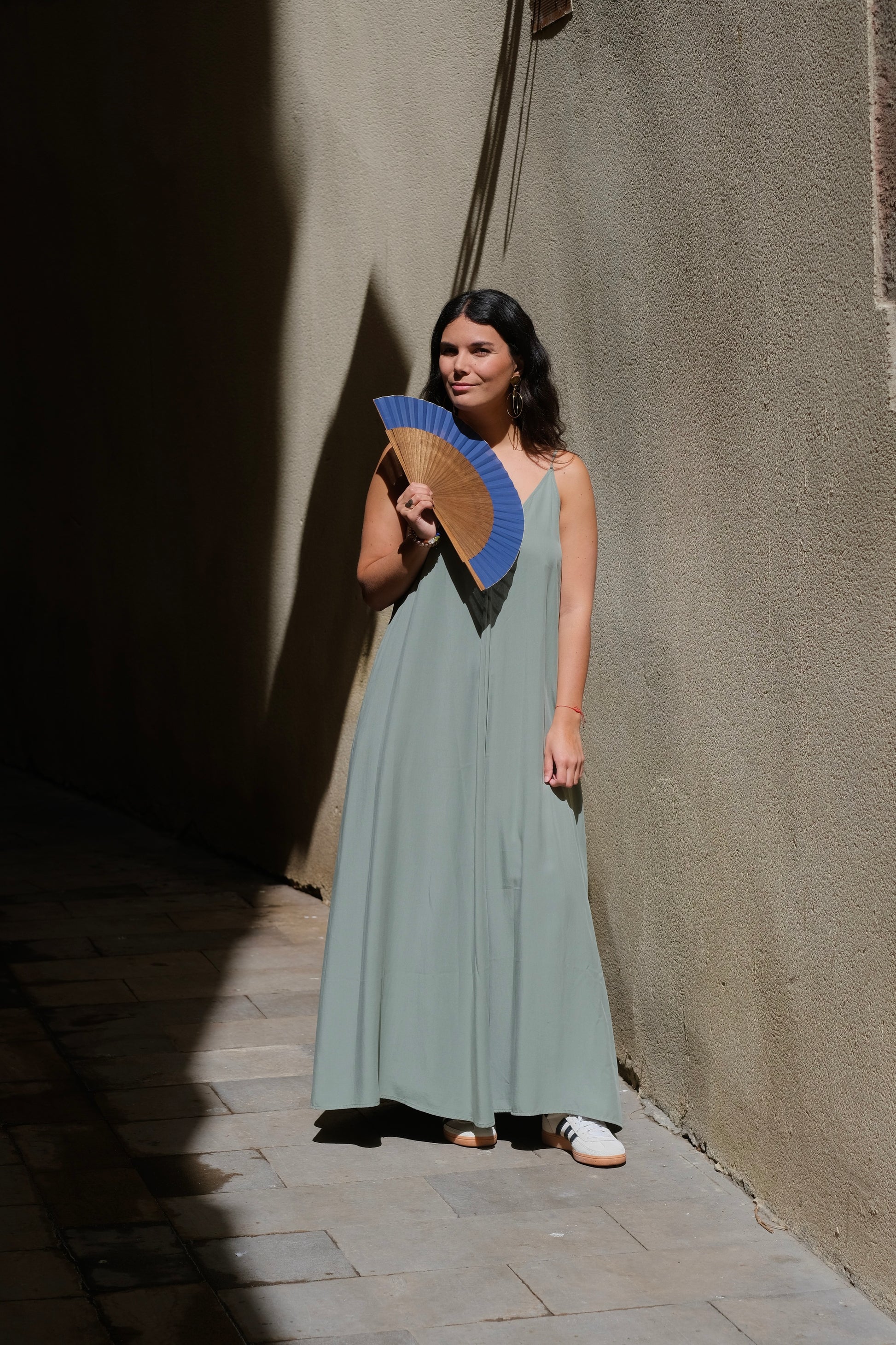 Mujer con vestido verde utilizando un abanico color azul marino. Marca rafega.