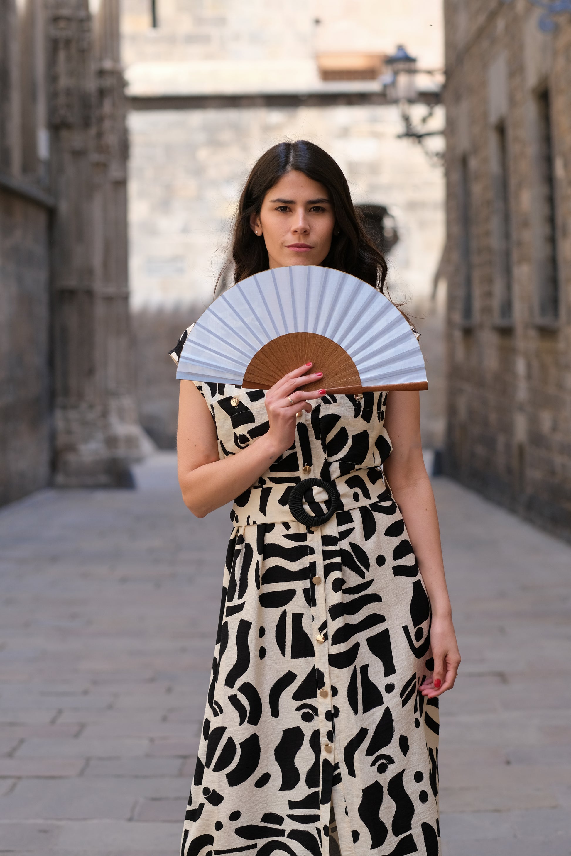 Mujer posando con abanico color azul en el barrio gótico, Barcelona. Lleva vestido de estampados beige y negro.