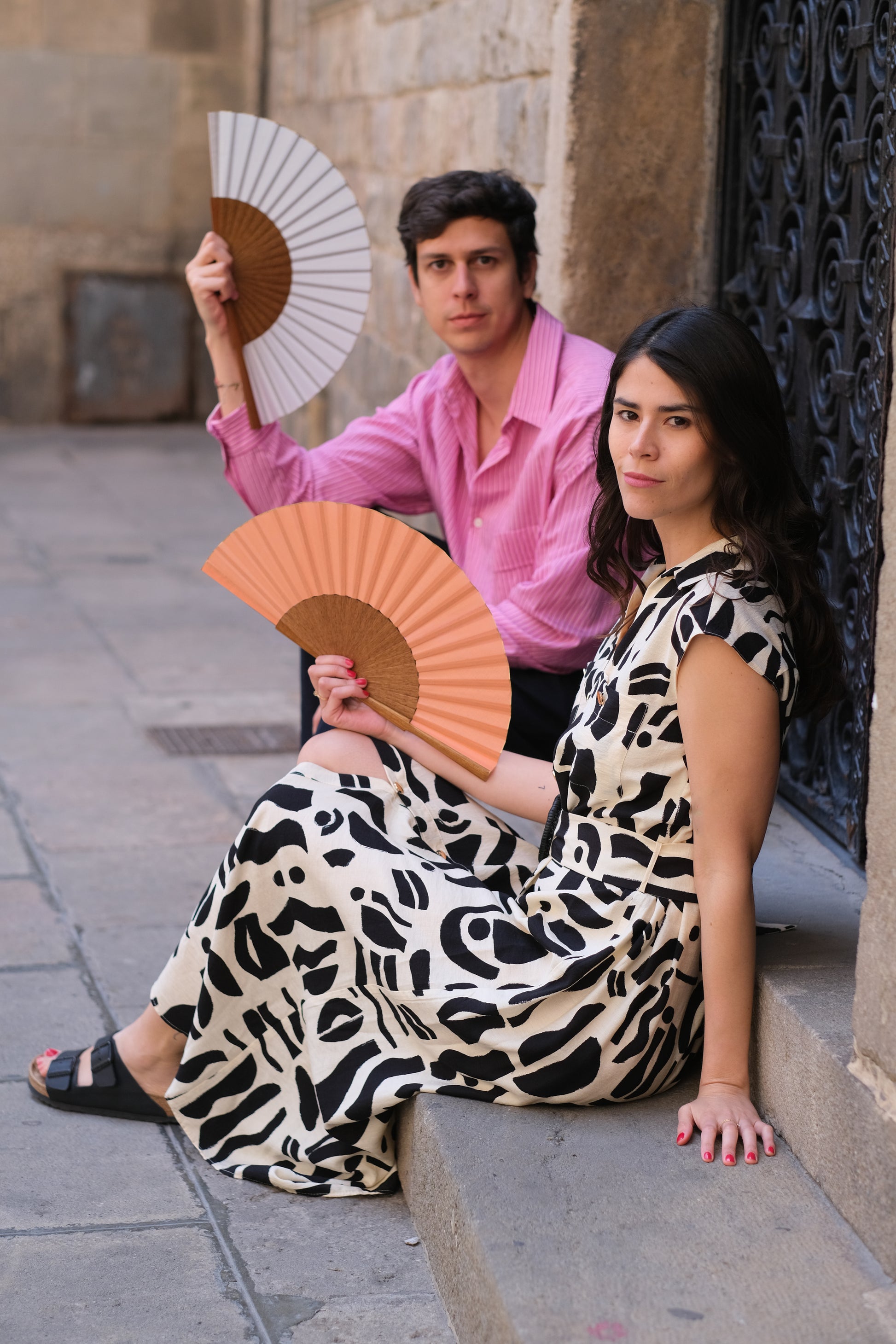 Hombre y mujer utilizando abanicos color rosa y blanco en Barcelona.